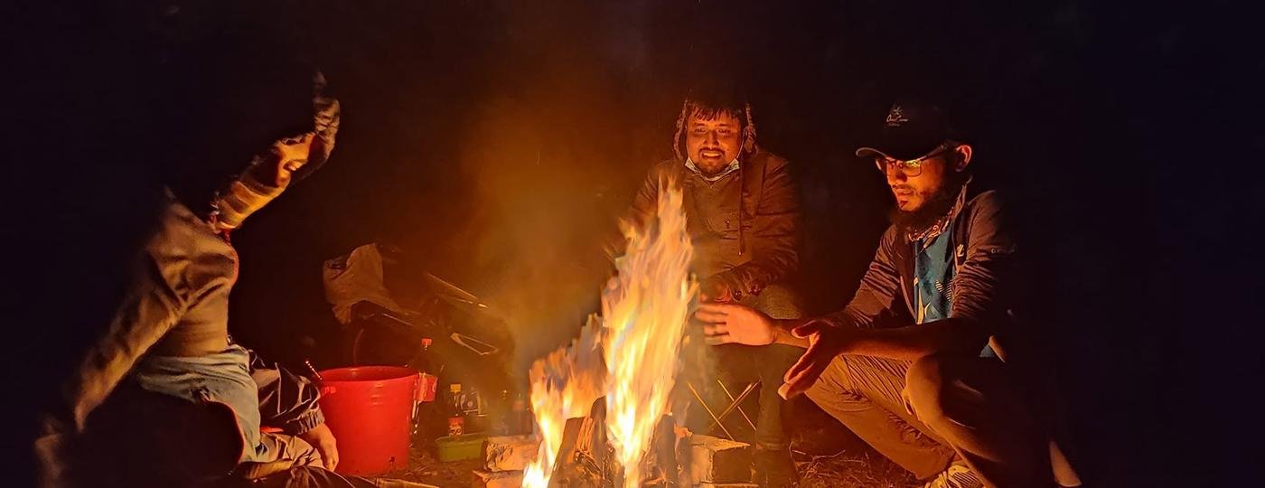 Friends warming their hands around a bonfire at night