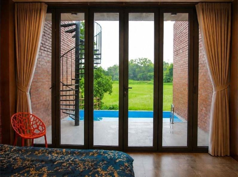 Cottage bedroom looking through glass doors to a private pool and rice fields