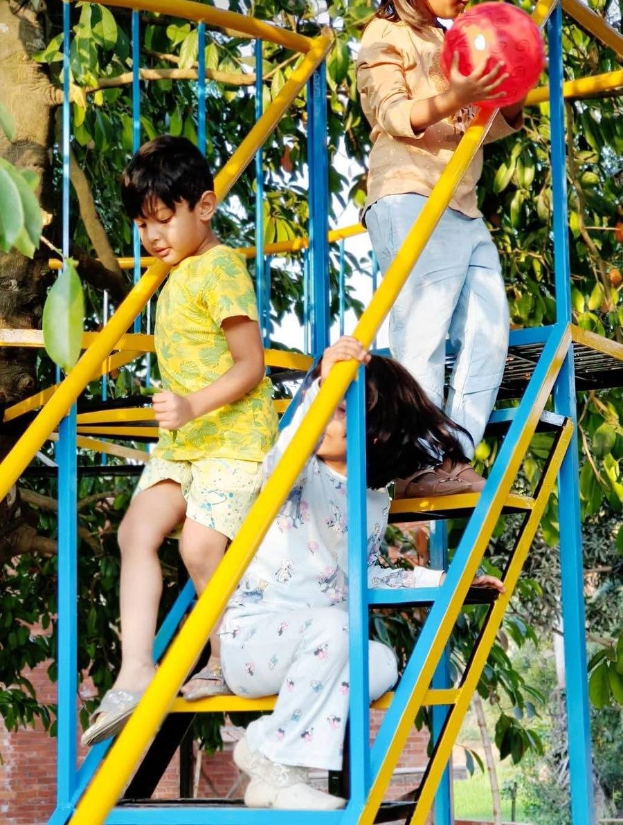 Children climbing a blue and yellow play tower under trees