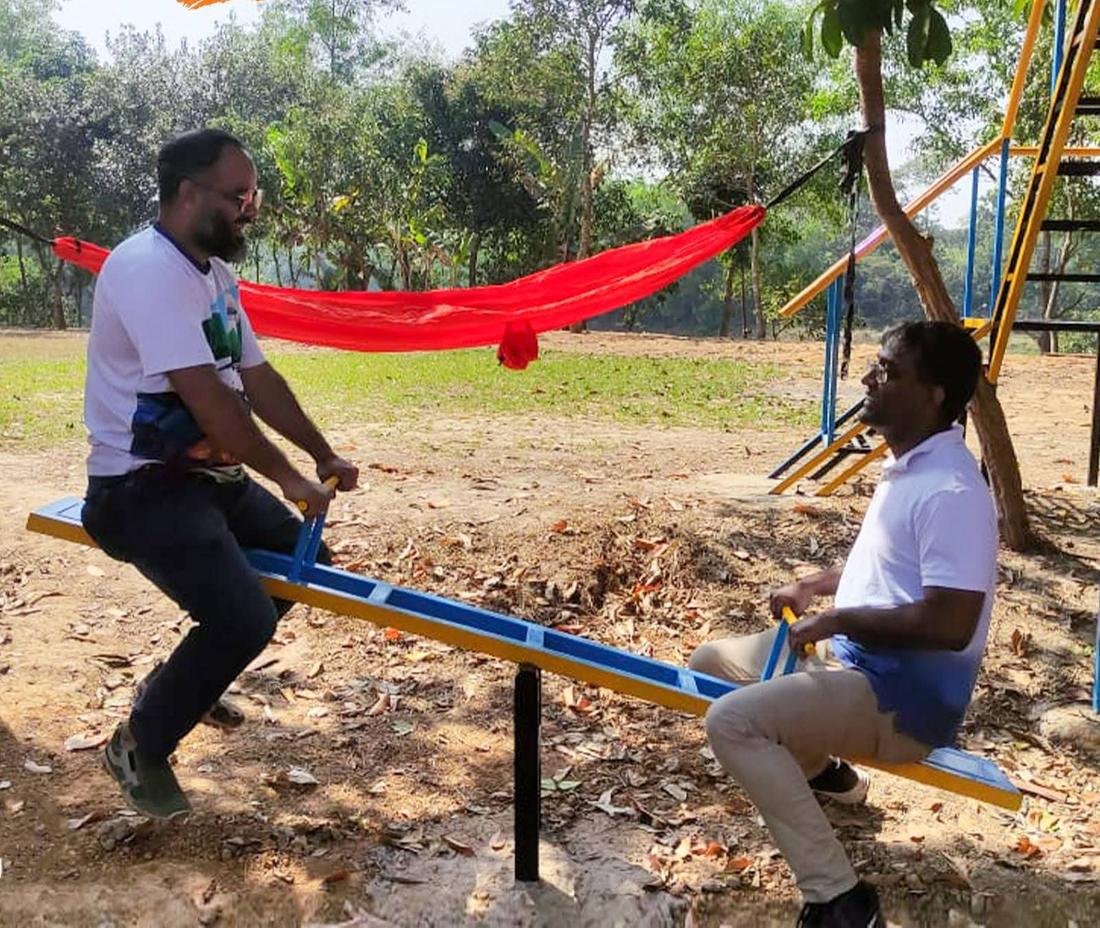 Two adults on a seesaw with a red hammock behind