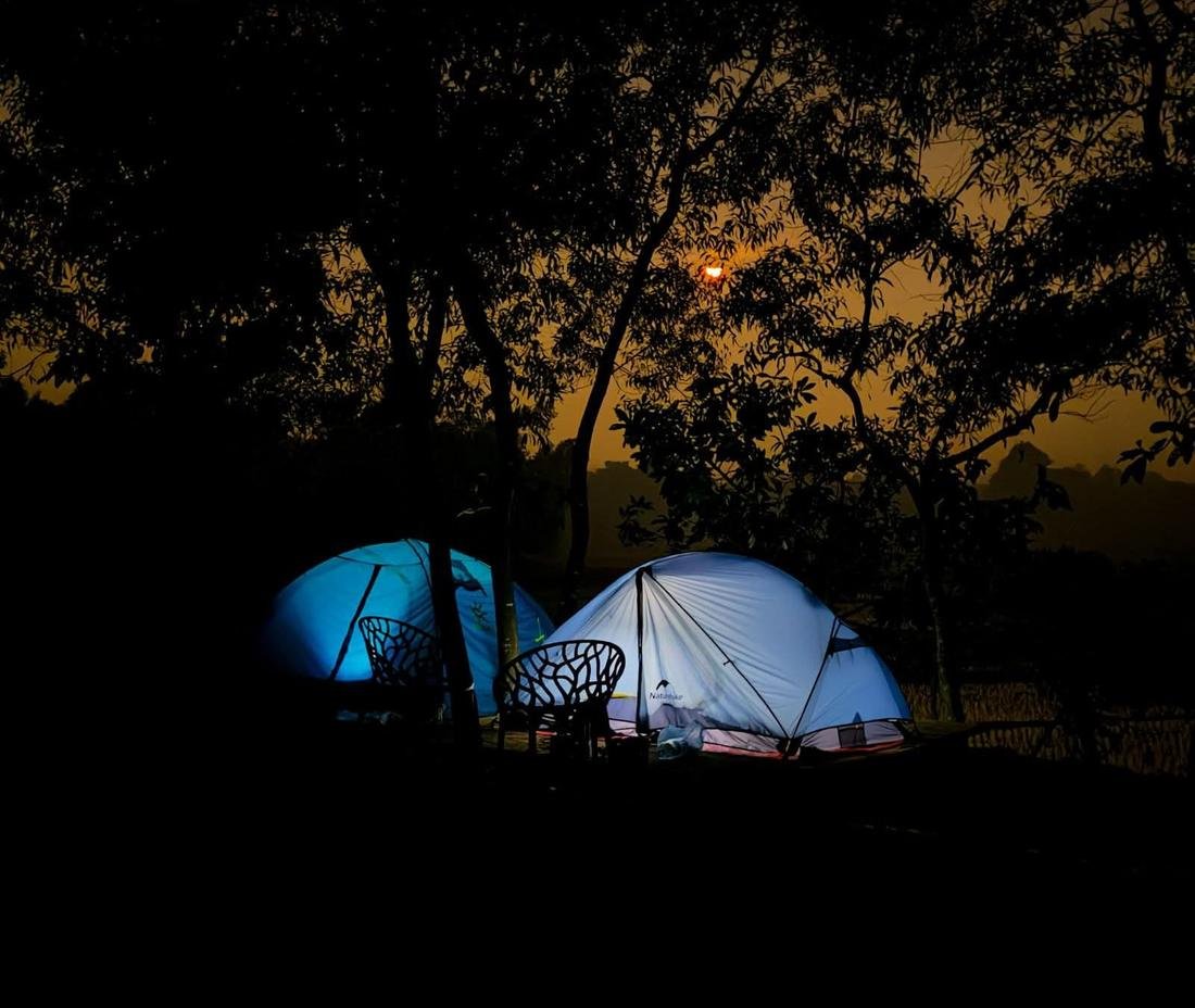 Two lit tents and chairs under trees at dusk